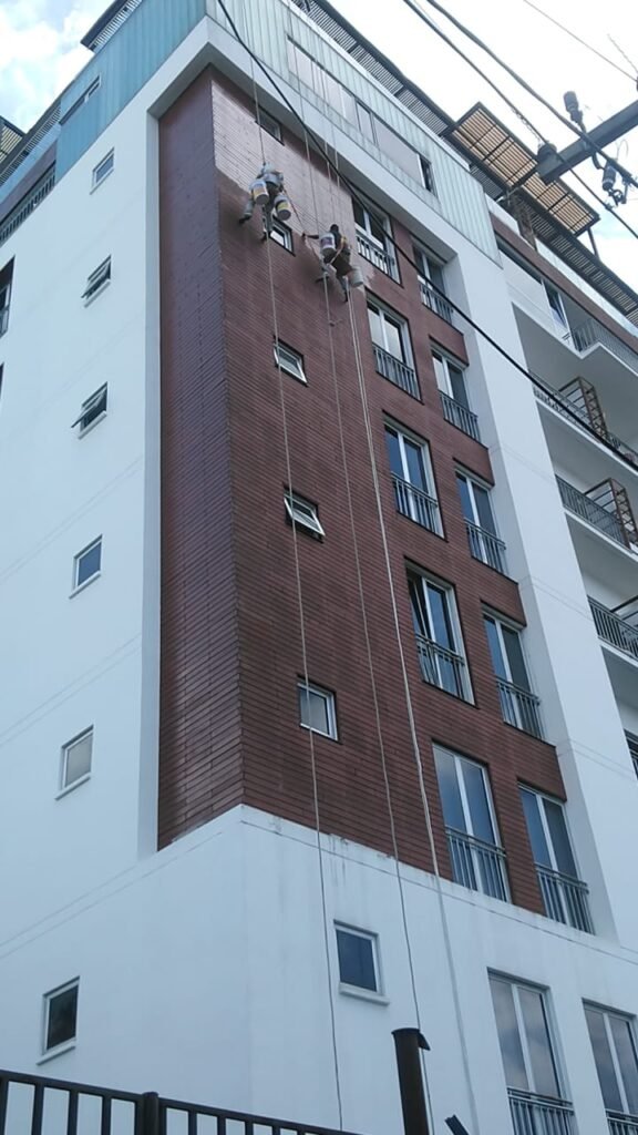 Aplicación de impregnante protector sobre elementos de madera en la fachada de un edificio de varios niveles.